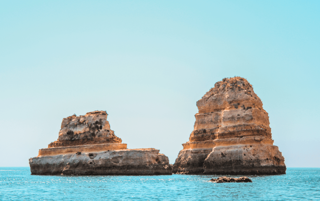 Two rock formations in the ocean under a clear blue sky.
