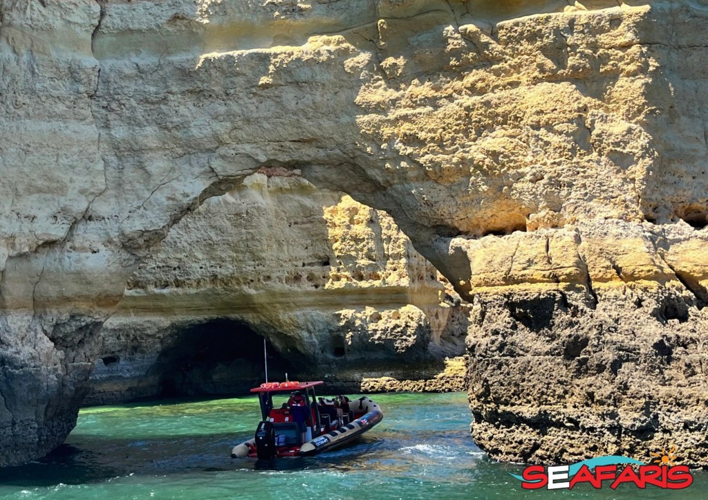 Boat passing under a natural rock arch in clear blue water.