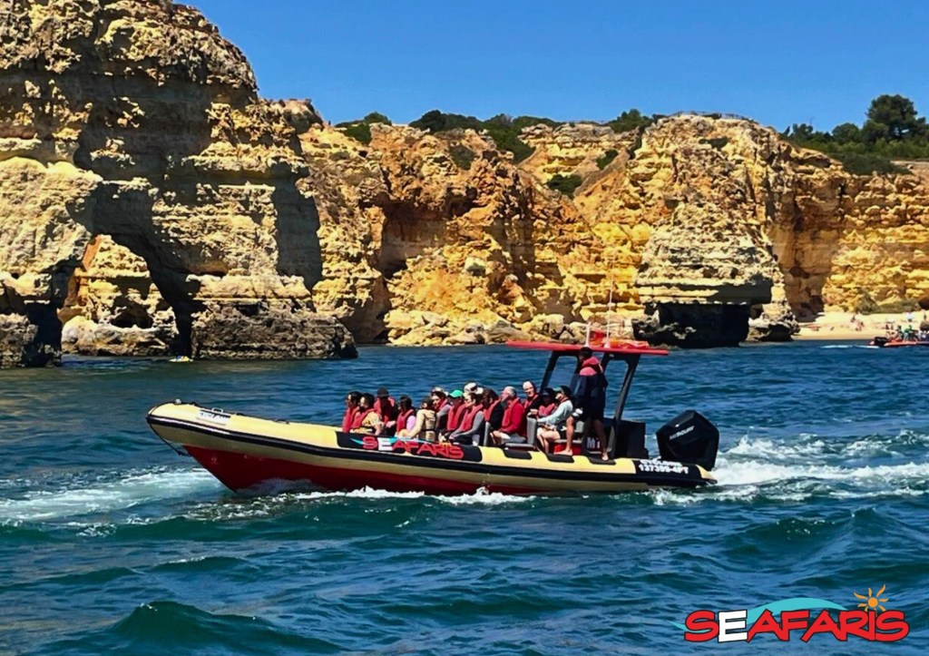 Tour boat with passengers in front of rocky cliffs on a sunny day.