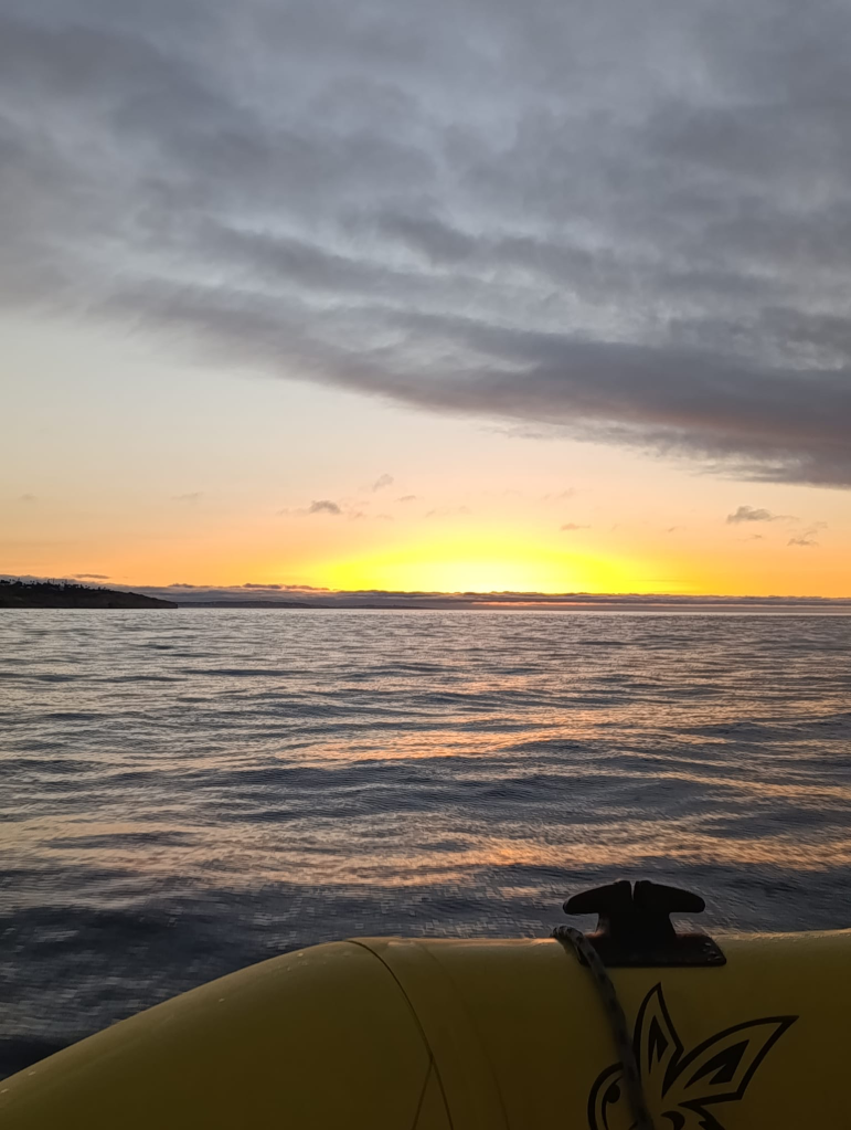 Sunset over calm ocean with dark clouds and a yellow boat in foreground.