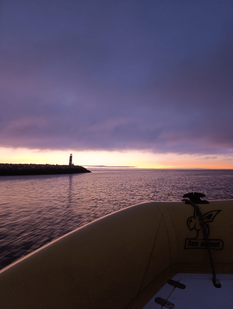 Sunset over ocean with lighthouse silhouette and boat edge visible.