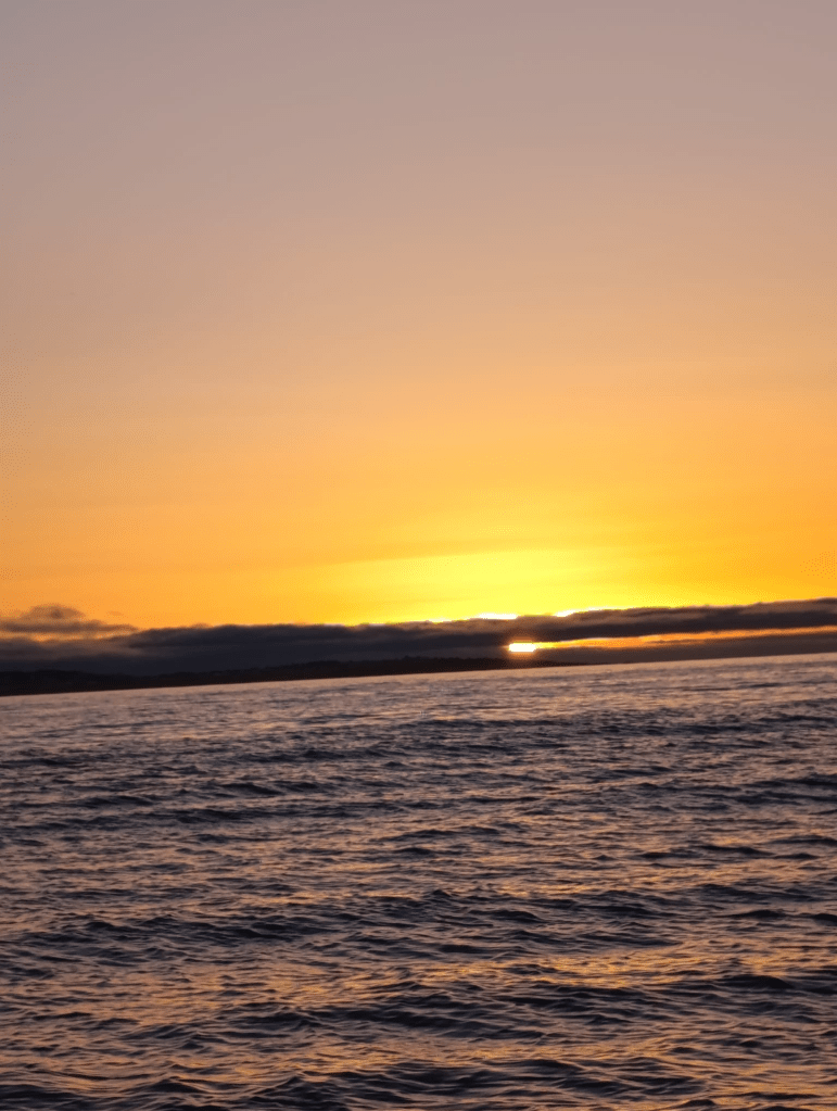Sunset over ocean with orange sky and rippling waves.