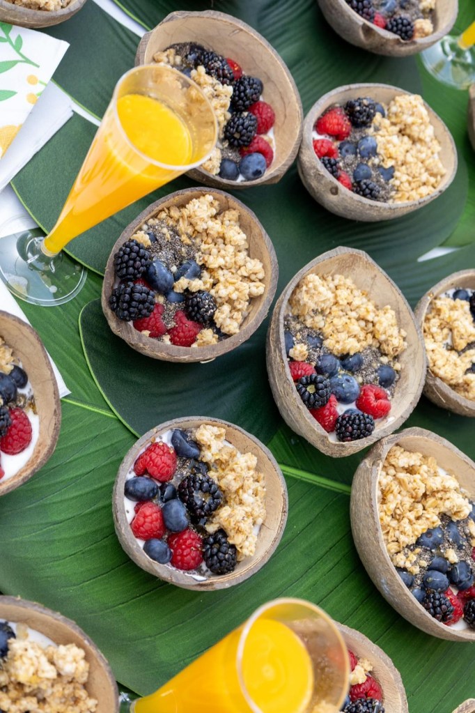 Coconut bowls with granola, berries, and mimosas on a leaf background.