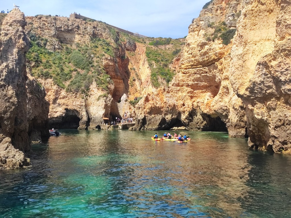 Kayakers in a rocky cove with clear blue water and cliffs.