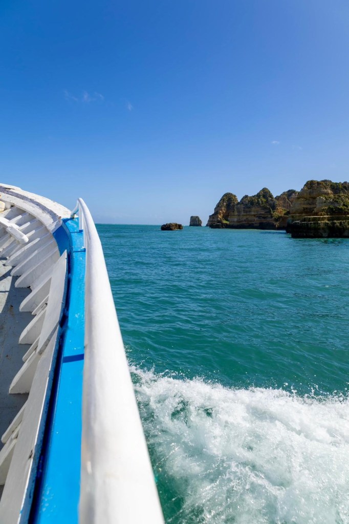 Boat on turquoise sea near rocky coastline under clear blue sky.