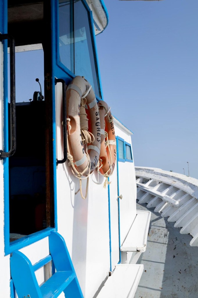 Side of a boat with lifebuoys hanging, clear blue sky above.