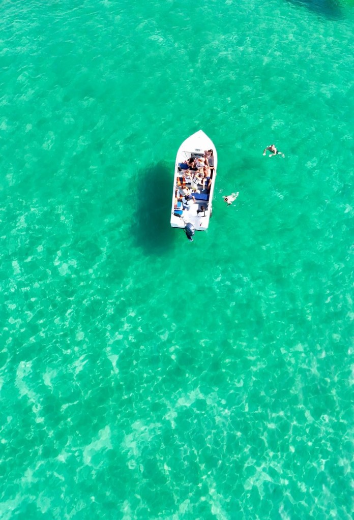 Aerial view of a boat on clear turquoise water with swimmers nearby.