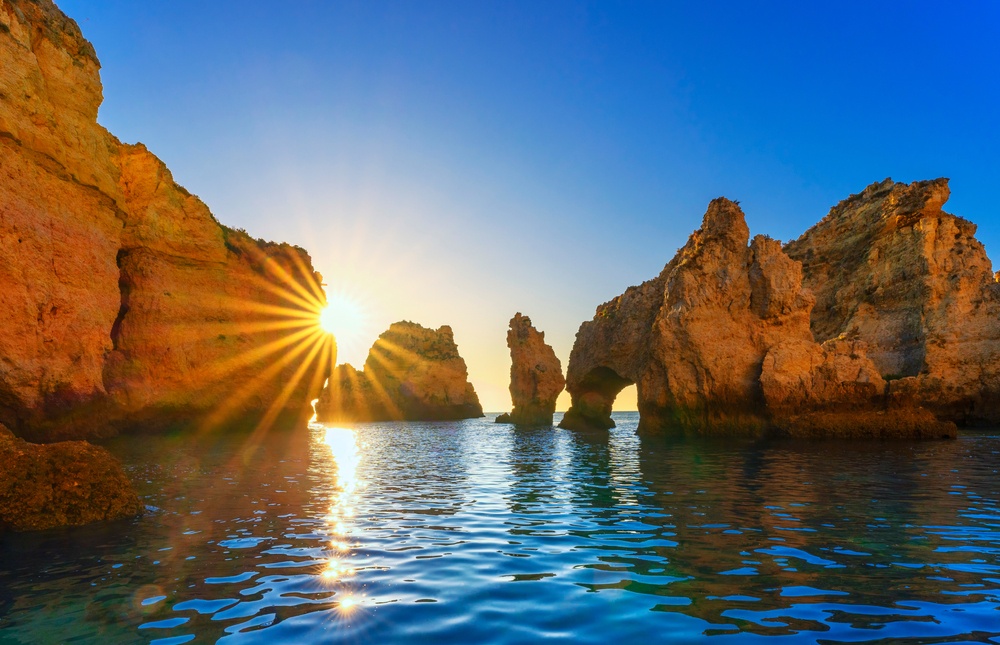 Sunset over rocky coastline with sun rays and calm sea.