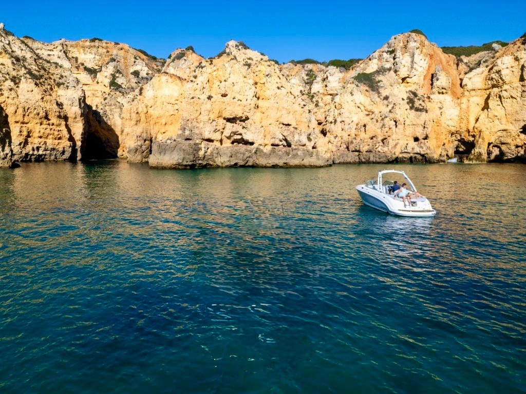 Boat on clear water near rocky cliffs under a blue sky.