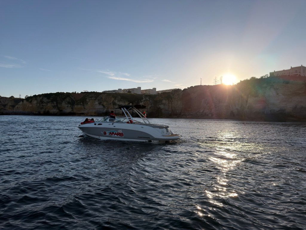 Boat on water near cliffs with sunset in the background.