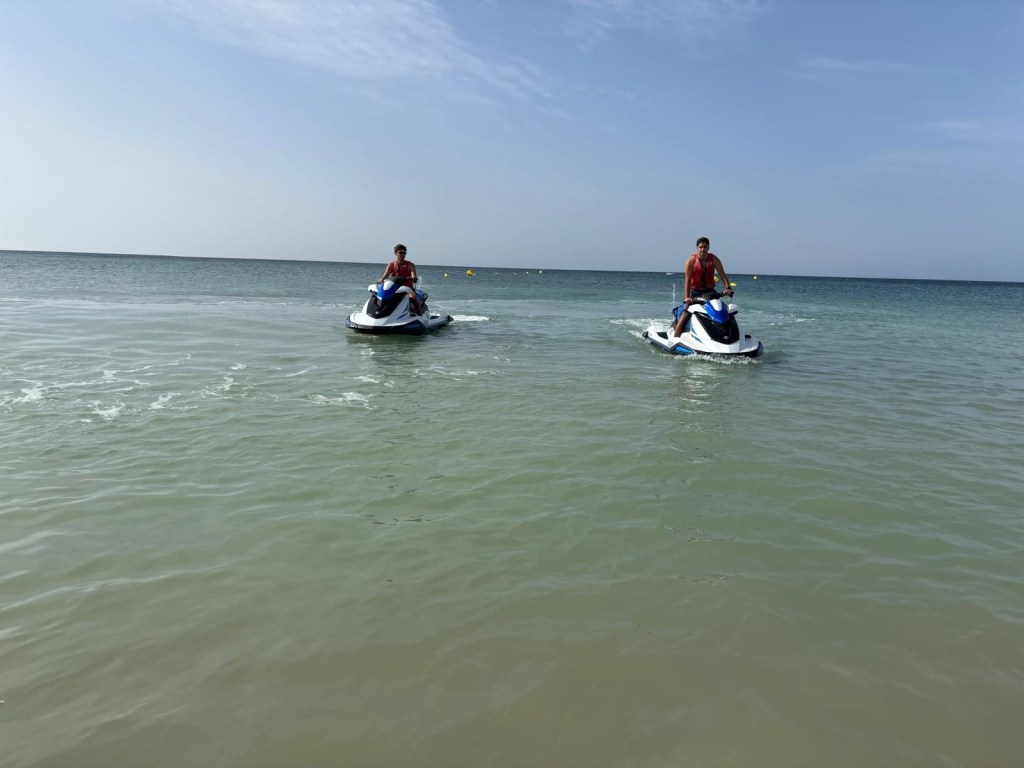 Two people riding jet skis on calm sea under a blue sky.