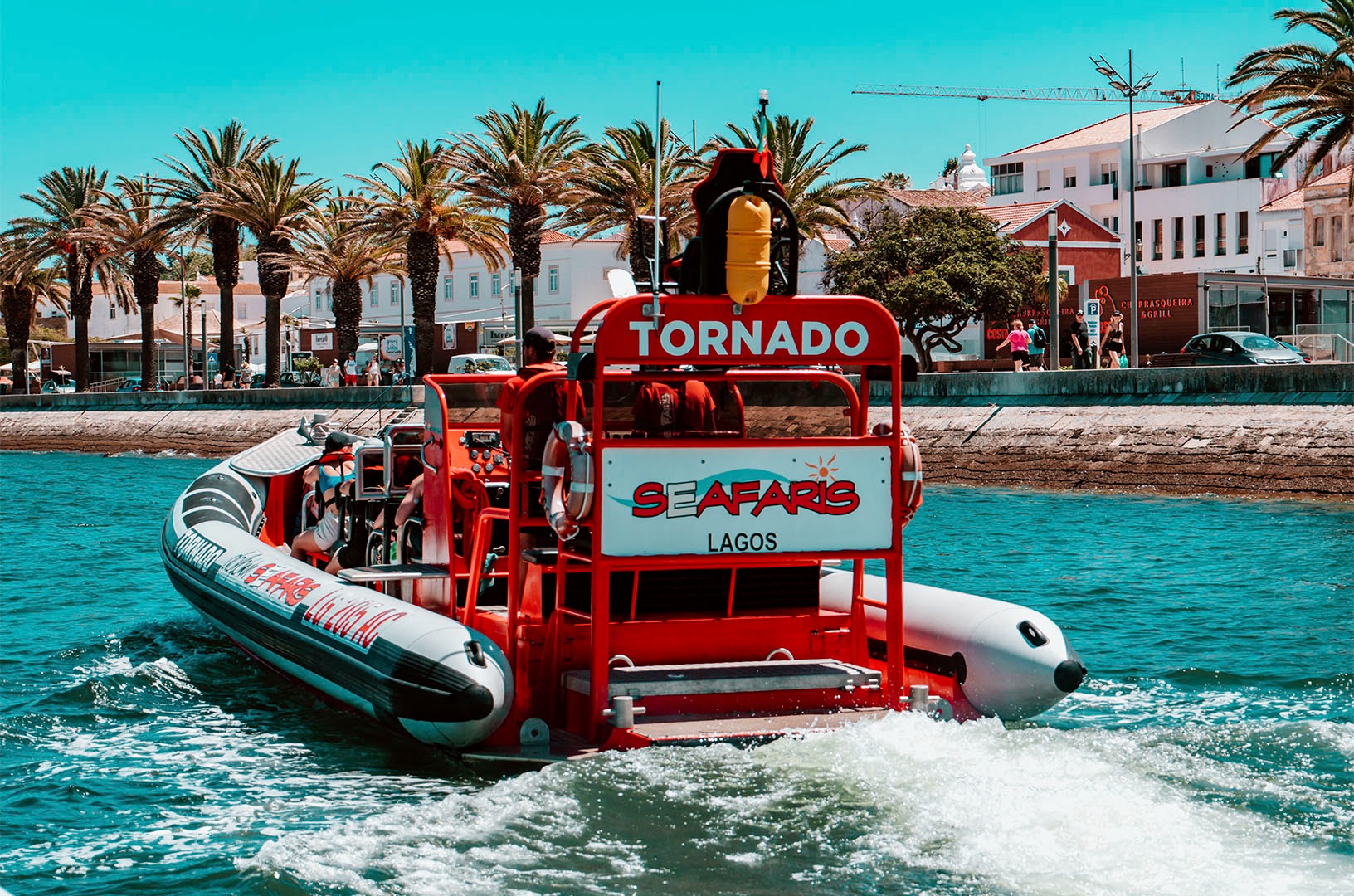 Red motorboat named Tornado on water near palm trees and buildings.