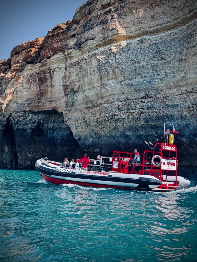 Red and white tour boat near steep rocky cliffs on blue water.