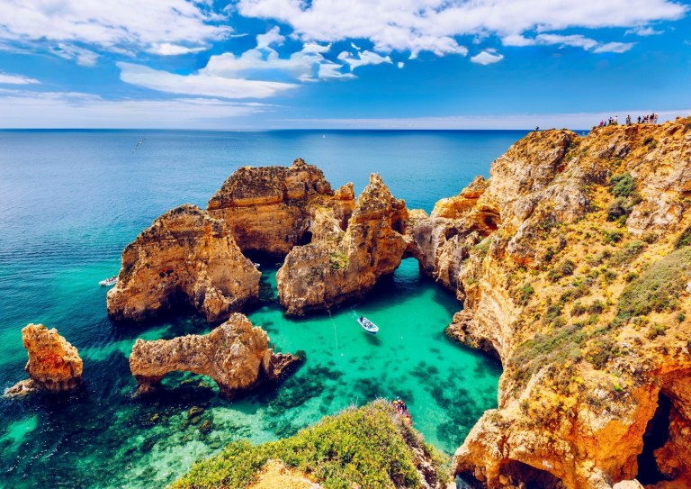 Scenic view of rocky cliffs and turquoise sea with a small boat, under a blue sky.