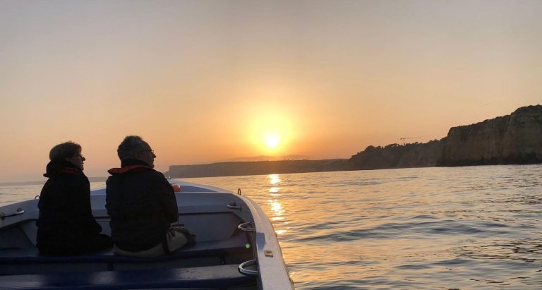 Two people on a boat watching a sunset over the ocean.